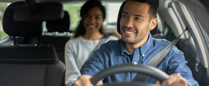 Happy Latin American rideshare driver transporting a woman in a car