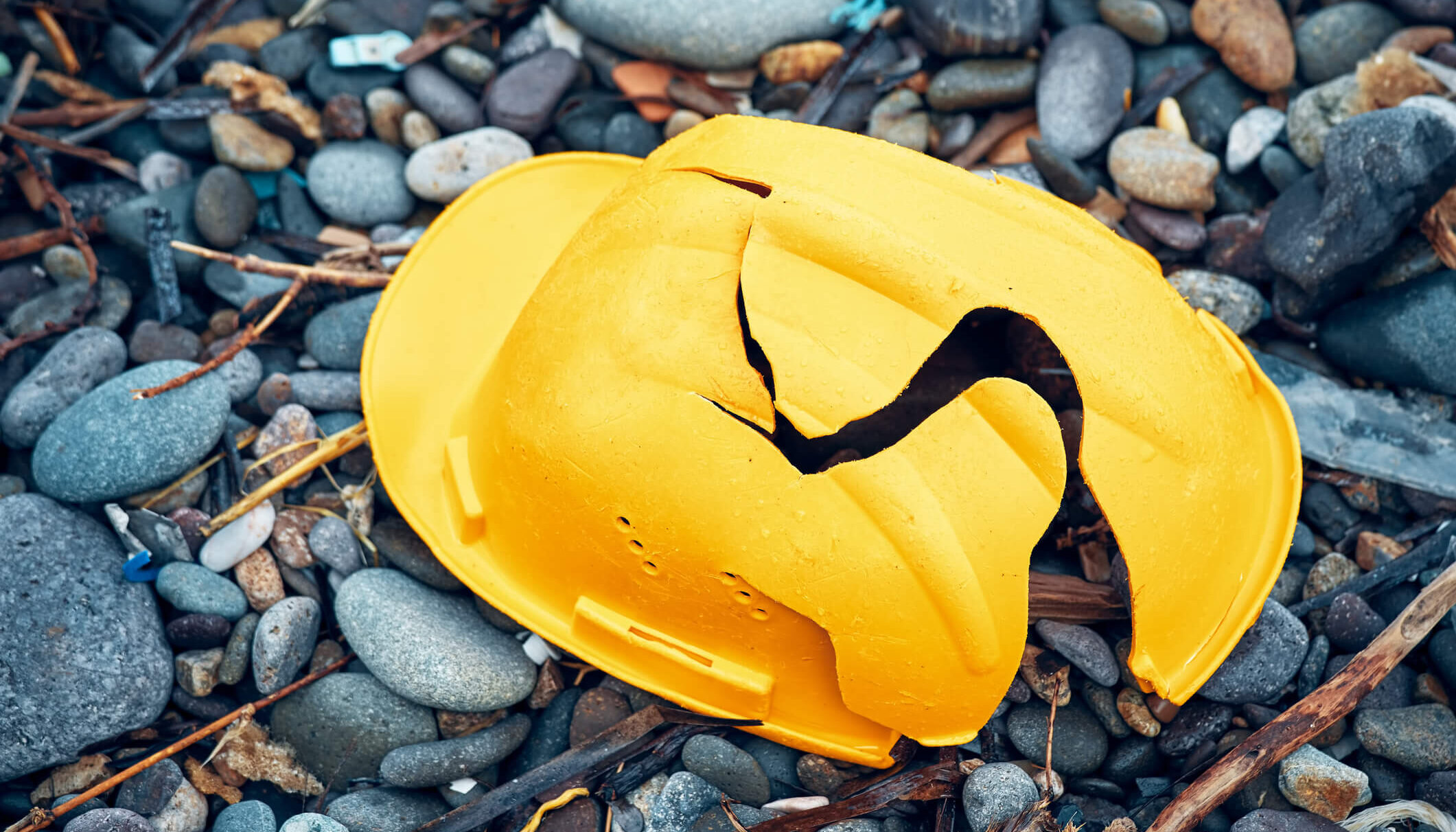 Cracked work helmet on the floor covered with pebble stones